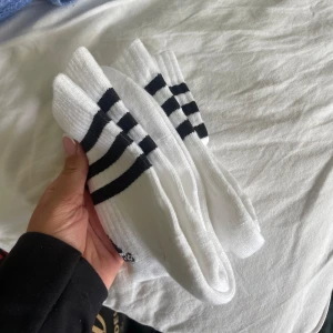 Vita sportiga långa strumpor från adidas  - Säljer 2-pack vita strumpor från adidas. Klassisk sportig look, perfekta till sneakers eller träning. Strumporna är ribbade och har en mjuk känsla.