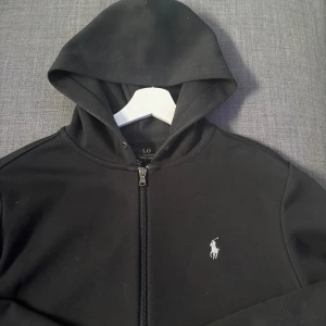 Svart zip-hoodie från Polo Ralph Lauren - Säljer en svart zip hoodie från Polo Ralph Lauren med dragkedja och vit broderad logga på bröstet. Tröjan är i storlek S och är i fint skick. Skicka ett meddelande om du undrar något!