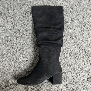 Svarta höga stövlar med klack - Säljer ett par svarta höga stövlar med bred klack och rund tå. Stövlarna är i mocka och har dragkedja på insidan. Perfekta för att lyfta en outfit under kallare månader.
