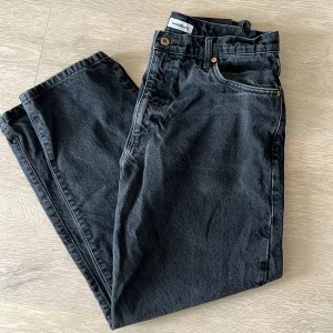 Svarta jeansbyxor från Woodbird - Snygga svarta jeansbyxor från Woodbird med klassisk femficksdesign och raka ben. Byxorna har knappgylf och bälteshällor, samt diskreta detaljer i kopparfärg vid fickorna. Perfekta för en stilren och avslappnad look. Storlek 30-31