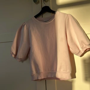 Ljusrosa puffärm tröja från Gina Tricot - Säljer en ljusrosa tröja från Gina Tricot med puffärmar och rund halsringning. Tröjan har korta ärmar med resår vid ärmslut och en rak passform. Perfekt för dig som gillar en söt och trendig stil.