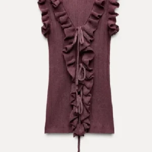 Topp med volang  - Superfin plommonlila topp med djup v-ringning, volangdetaljer längs kanten och knyt framtill. Toppen är ribbad och ärmlös, perfekt för att lyfta din outfit med en romantisk touch. Helt slutsåld med prislapp kvar