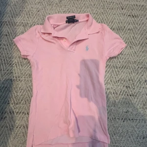 Rosa pikétröja från Ralph Lauren - Säljer en klassisk rosa pikétröja från Ralph Lauren i modellen The Skinny Polo. Tröjan har korta ärmar, krage och knäppning framtill samt den ikoniska broderade loggan på bröstet. Tillverkad i 100% bomull.
