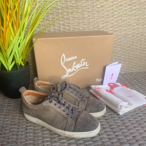 Loubs  - Säljer ett par mörk gröna sneakers från Christian Louboutin med klassisk röd sula och snörning. Skorna har rund tå och är tillverkade i mocka med detaljer i skinn. Kommer med originalkartong och dustbags.