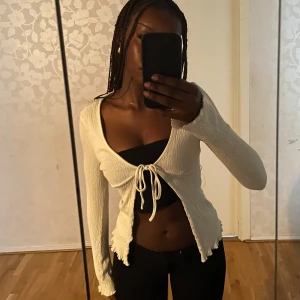 Vit ribbad croppad knyt-topp från bikbok - Säljer en vit croppad topp med långa ärmar och ribbad struktur. Toppen har knytning framtill och vågiga kanter vid ärmslut och nederkant. Knappt använd och kan vara as snygg över en klänning eller en lager-på-lager outfit‼️😍Säljs pga det inte är min stil längre💛💛