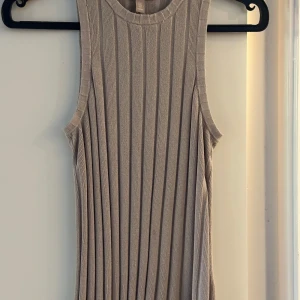Beige ribbad ärmlös klänning - Säljer en beige ribbad topp med ärmlös design och rund halsringning. Toppen har en rak passform och är tillverkad i ett mjukt, stretchigt material som ger en snygg siluett. Perfekt för en stilren och enkel look. Detta är en fin topp köpt på HM i storlek L