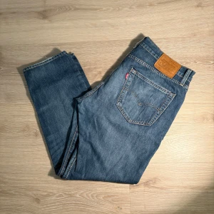 Levis 502 blå jeansbyxor - Klassiska blå Levis 502 jeans med rak passform och femficksdesign. Byxorna har en brun läderpatch bak i midjan och den ikoniska röda Levis-taggen på bakfickan. Perfekta för en tidlös och avslappnad stil. 32/30
