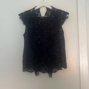 Mörkblå spetsblus från Zara - Supersnygg mörkblå blus från Zara i spets med blommigt mönster. Blusen är ärmlös med volangdetaljer längs axlarna och knäpps i nacken. Perfekt för att klä upp sig till en middag eller fest!  