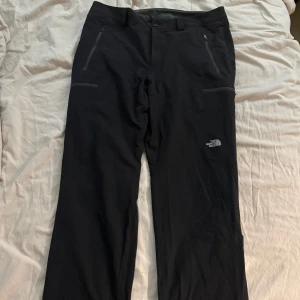 Svarta byxor från The North Face - Svarta byxor The North Face med raka ben och dragkedjeförsedda fickor framtill. Byxorna har en stilren look med diskret logga på benet och är perfekta för kalla dagar eller utomhusaktiviteter. Storlek M. 