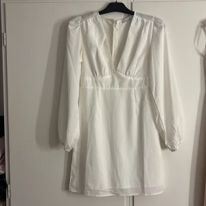 Fin vit kortklänning  - Superfin vit kortklänning från Nelly x Glamorous med v-ringning, långa puffärmar och dragkedja bak. Klänningen har en lätt och flowy känsla, perfekt för dig som vill ha en stilren och trendig look.