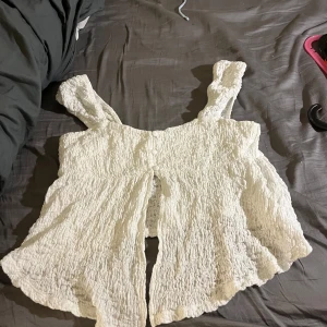 Vit linnetopp från Gina - Supersöt vit linnetopp från Gina Tricot med breda axelband och smockad struktur. Toppen har knappar framtill och en lätt utsvängd passform som ger en luftig känsla. Perfekt för varma dagar och enkel att styla med jeans eller kjol. Andvänd ca 2ggr