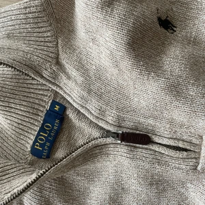 Beige stickad half zip från Polo Ralph Lauren - Säljer en beige stickad tröja från Polo Ralph Lauren med half zip och klassisk broderad logga på bröstet. Tröjan har ribbade muddar och krage, lång ärm och en relaxed passform. Perfekt för lager-på-lager och chill dagar.