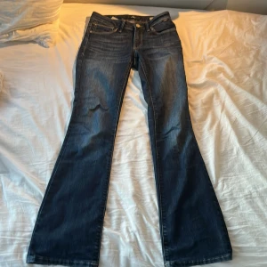 Mörkblå bootcut jeans från Mavi - Snygga mörkblå jeans från Mavi med klassisk bootcut-passform. Jeansen har fem fickor, kontrastsömmar och en stilren tvätt. Tillverkade i mjukt denimtyg som sitter skönt hela dagen. Perfekta för dig som gillar en tidlös look med lite extra vidd nertill. Lite slitna längst ner till. Obs kan skicka som tidigast den 8e augusti!
