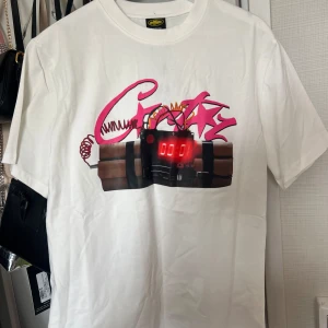 Vit t-shirt från Corteiz - Vit t-shirt från Corteiz med färgstark print framtill som visar en tecknad bomb med digital display och rosa graffiti-text. Baksidan har stor svart text 'NOTIME4LUV'. Klassisk passform och rund hals. Perfekt statement-plagg för dig som gillar streetwear vibes. Det bara skriva om du vill ha fler bilder och priset kan alltid diskuteras. Skickas inom 1-2 dagar.