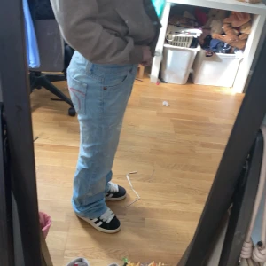 Ljusblå bootcut/baggy  jeans från Gina Tricot - Säljer ett par ljusblå jeans från Gina Tricot i klassisk bootcut-modell. Jeansen har röda detaljer på bakfickorna, rosa sömmar och en snygg knapp framtill. Tillverkade i bomull med en relaxed passform och normal midja. Perfekta för en chill och trendig look. Dom är helt slutsålda och säljs inte längre i affärer eller hemsidan. Den har inga defekter alls men som man ser på bilderna säljer jag dessa för att de är för stora och långa på mig! Behövs fler bilder så är det bara att skriva! 🩷🩷