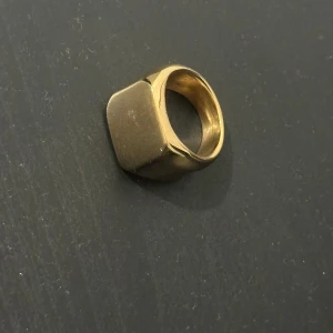 Chunky guldfärgad signetring - Stilren och chunky signetring i guldfärg med en fyrkantig platt topp. Ringen har en modern och minimalistisk design som sticker ut och passar perfekt för dig som gillar statement-smycken. Perfekt accessoar för att lyfta din outfit.