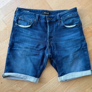 Blå jeansshorts från Jack & Jones - Snygga blå jeansshorts från Jack & Jones i regular fit. Klassisk femficksmodell med uppvikta benslut och detaljerade sömmar. Perfekta för sommardagar och har en cool, avslappnad vibe. Gjorda i mjukt denimtyg som är skönt att bära.