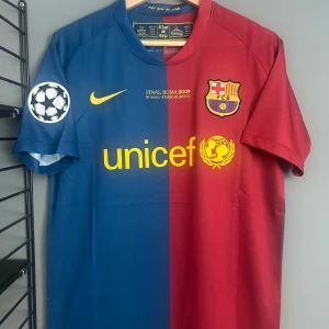 FC Barcelona Henry 14 Final Roma 2009 tröja - Säljer en ikonisk FC Barcelona fotbollströja från Champions League-finalen 2009 med Henry 14 på ryggen. Tröjan är halva blå, halva röd med gula detaljer, klubbmärke och Nike-logga. Tillverkad i lätt och ventilerande Dri-Fit-material. Champions League-märke på ärmen. Helt ny med tagg en replika med tagg 