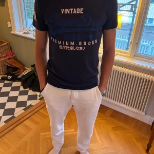 Superdry t-shirt med tryck - Snygg mörkblå t-shirt från Superdry med stort tryck framtill och textdetaljer på ärmen. Använd ett fåtal gånger! Model är 183cm & 75kg. Bara att skriva om ni har frågor!