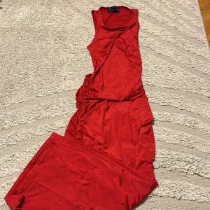 Röd långklänning med rynkade detaljer - Snygg röd långklänning från NA-KD med ärmlös design och rynkade detaljer längs sidorna och bak. Klänningen har en figurnära passform och är tillverkad i ett mjukt, stretchigt material som ger en cool och trendig look.