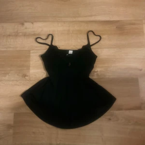 Svart lace mesh babydoll - Svart linnetopp med tunna axelband och v-ringning dekorerad med spets. Toppen har en liten guldfärgad detalj framtill och lätt utställd nederdel. Perfekt för dig som gillar en feminin och vintage look