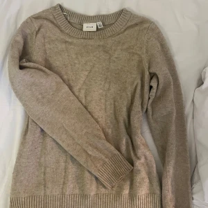 Beige stickad tröja från Vila - Mysig beige stickad tröja från Vila med rund halsringning och ribbade muddar vid ärmslut och nederkant. Perfekt för lager-på-lager och chill höst- eller vinterstil. Enkel och stilren design som funkar till det mesta.