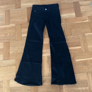 Svarta flare jeans från Cheap Monday - Svarta flare jeans från Cheap Monday med låg midja. Byxorna har klassisk femficksdesign och är tillverkade i en stretchig bomullsblandning för skön passform. Snyggt utsvängda ben och coola detaljer med rosa logga på bakfickan.