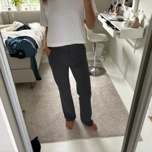 Mörkgrå kostymbyxor med raka ben - Säljer ett par mörkgrå kostymbyxor med raka ben och klassisk passform. Byxorna har hällor för bälte, diskreta fickor och stängs med dragkedja och knapp. Perfekta för en clean och stilren look.