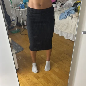 Svart ribbad midikjol från H&M - Säljer en svart ribbad midikjol från H&M i storlek XS. Kjolen är figurnära och har en stretchig passform som sitter snyggt på kroppen. Perfekt att styla med en crop top eller oversized hoodie för en chill vibe.