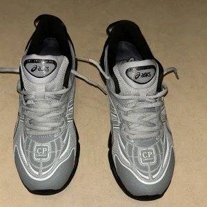 ASICS x C.P. Company Gel-Quantum 360 - Grå och svarta sneakers från ASICS i samarbete med C.P. Company. Modellen är Gel-Quantum 360 med mesh- och syntetmaterial, tydliga vita detaljer och loggor på tungan och hälen. Skorna har snörning och en chunky svart sula för extra komfort och streetkänsla.helt oanvänd mötts upp i goteborg!