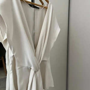 Vit blus från zara - Supersnygg vit blus från Zara knyt framtill. Blusen har v-ringning, ärmlös design och är tillverkad i ett mjukt, lätt material som ger ett elegant fall. Perfekt för dig som gillar stilrena och fräscha looks.