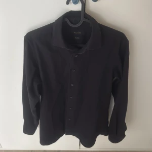 Marinblå skjorta från Massimo Dutti - Stilren marinblå skjorta från Massimo Dutti i 100% bomull. Klassisk krage, långärmad och med knappar framtill. Perfekt för dig som gillar en clean och enkel look. Skjortan har en normal passform och är riktigt skön att bära.