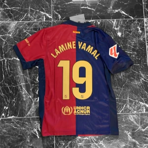 FC Barcelona Lamine Yamal tröja Nike S - Säljer en officiell FC Barcelona matchtröja från Nike med Lamine Yamal och nummer 19 på ryggen. Tröjan har klassiska blå och röda vertikala fält, klubbmärke på bröstet, gul Nike-logga och tryck i gult. Kortärmad modell i lätt funktionsmaterial.