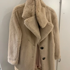 Beige pälsjacka från Zara Woman - Säljer en supermjuk och fluffig beige pälsjacka från Zara Woman. Jackan har stora slag, knappar framtill och är helfodrad i ljusrosa tyg. Perfekt för att hålla sig varm och snygg under kyliga dagar. Jackan har en klassisk och oversized look.