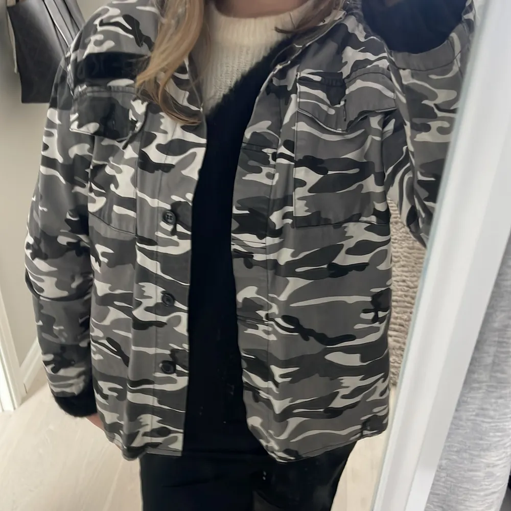 Säljer en cool camouflagejacka med knappar. Jackan har en avslappnad passform och är perfekt för en streetwear-look. Den har långa ärmar och flera fickor framtill.. Takit.