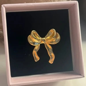 Guldfärgad ring med rosett - Elegant guldfärgad ring med en dekorativ rosett. Perfekt för att ge en stilfull touch till din outfit. Justerbar storlek för att passa de flesta fingrar.