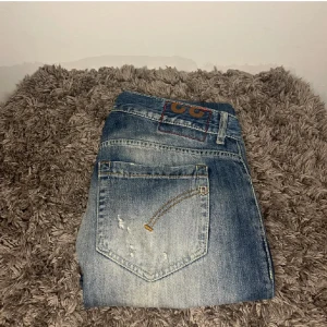 Dondup George - Snygga blå jeans från Dondup med slitna detaljer och en klassisk femficksdesign. Jeansen har en straight passform och är perfekta för en avslappnad stil. De har en dragkedja och knapp framtill.