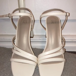 Gräddvita/ beigea klackskor med bred klack - Eleganta klackskor med smala remmar. Perfekta för en stilren look med justerbart spänne runt ankeln. Passar perfekt vid student eller för att klä upp outfit, endast använda en gång vid en studentfest. 