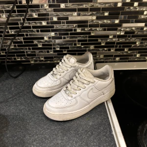 Vita Nike Air Force sneakers - Säljer ett par klassiska vita Nike Air Force sneakers. De har en stilren design med snörning och perforerade detaljer på ovansidan för extra ventilation. Perfekta för en casual look.