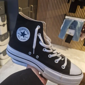 Svarta Converse All Star sneakers - Klassiska svarta Converse All Star sneakers med vit lite högre sula och snörning. Skorna har den ikoniska logotypen på sidan och är perfekta för en avslappnad stil.