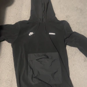 Svart hoodie från Nike Air Max - Säljer en svart hoodie från Nike Air Max med justerbar huva och stor ficka framtill. Perfekt för en sportig look eller avslappnade dagar. Den har Nike-loggan och Air Max-märke på bröstet.