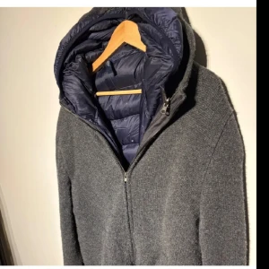 Gran sasso cardigan  - Grå gran sasso cardigan med en avtagbar dunväst på insidan. Mycket bra skick förutom ett litet hål på insidan av dunvästen men inget som syns och högra sidan av nametaggen har ramlat av men kan enkelt fixas. Storlek 56 motsvarar Xl 