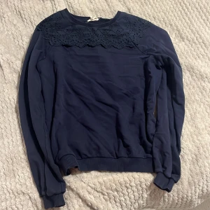 Mörkblå tröja med spetsdetaljer - Säljer en snygg mörkblå tröja med spetsdetaljer runt halsen. Tröjan har långa ärmar och ribbade muddar vid ärmslut och nederkant. Perfekt för en stilren look. Storlek S. 65% bomull, 35% polyester. Använd men syns ej mycket. Hör av dig för eventuella frågor 🌸kolla gärna in mina andra annonser!⤵️✨