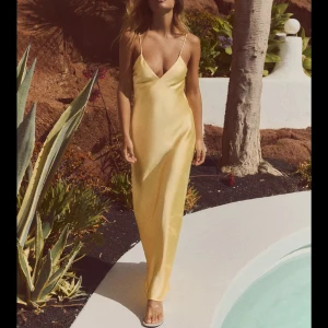 Gul långklänning med öppen rygg - Säljer en elegant gul långklänning i satin med smala axelband och djup v-ringning. Klänningen har en öppen rygg med dekorativa banddetaljer. Perfekt för bal! Detta är den populära klänningen från Zara som är slutsåld, aldrig använd med prislapp kvar! 