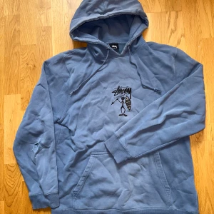Blå hoodie från Stüssy - Säljer en snygg faded blå hoodie från Stüssy med deras ikoniska logga på bröstet. Tröjan har en bekväm passform med långa ärmar och en praktisk magficka. Perfekt för en avslappnad stil. Hör av dig vid intresse! 