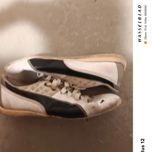 Vita och svarta sneakers från Puma - Säljer ett par vita och svarta sneakers från Puma. Skorna har en klassisk design med snörning och Puma-loggan på hälen. Perfekta för en sportig look.