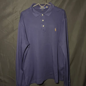Ralph Lauren Långärmad piké | Marinblå | Slim Fit | Stl L - Läs nedan för mer info!😊  Säljer en stilren mörkblå pikétröja från Ralph Lauren i slim fit. Tröjan har långa ärmar och klassisk krage med knappar. Den ikoniska broderade loggan syns på bröstet. Perfekt för en avslappnad men ändå elegant look.  Produktinformation:  ✅ Märke: Ralph Lauren  ✅ Storlek: L ✅ Färg: Marinblå ✅ Material: Bomull ✅ Passform: Slim fit ✅ Skick: Mycket bra skick, knappt använd  Frakt och betalning: 📦 Snabb leverans – skickar inom 1-2 dagar efter beställning📦