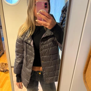 Grå dunjacka - Jackan är trekvartsärmad och mörkgrå samt lila inuti. Perfekt till våren!