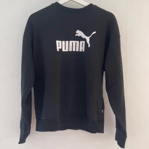 Svart sweatshirt från Puma - Säljer en svart sweatshirt från Puma med deras ikoniska logga i vitt på bröstet. Tröjan har långa ärmar och en klassisk rund halsringning. Perfekt för en avslappnad stil.