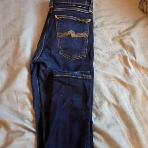 Mörkblå jeans från Nudie Jeans - Snygga mörkblå jeans från Nudie Jeans med klassisk femficksdesign och kontrasterande sömmar. De har en normal passform och är perfekta för en stilren look. Märkeslogga på baksidan.